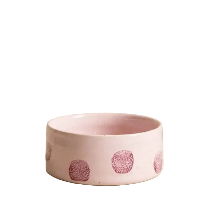 A light pink ceramic pet bowl with a pattern of dark pink textured polka dots, set against a minimalist beige background.